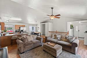 Living area featuring vaulted ceiling, wood finished floors, a ceiling fan, and a textured ceiling