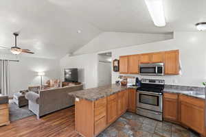 Kitchen with appliances with stainless steel finishes, open floor plan, a peninsula, lofted ceiling, and dark countertops