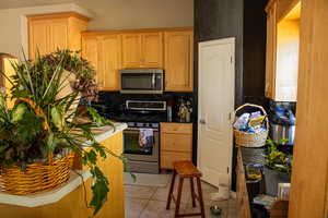 Kitchen featuring stainless steel appliances, tasteful backsplash, light tile patterned flooring, and light brown cabinets