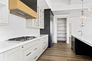 Kitchen featuring ventilation hood, stainless steel gas stovetop, light countertops, glass insert cabinets, and hanging light fixtures
