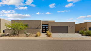 Pueblo revival-style home with an attached garage, concrete driveway, and stucco siding