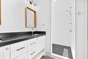 Bathroom featuring tiled shower, vanity, and wood finished floors
