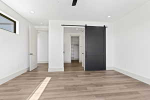 Unfurnished bedroom featuring a barn door, recessed lighting, light wood-style flooring, and ceiling fan