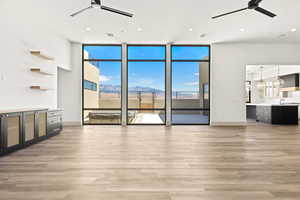 Unfurnished living room featuring a ceiling fan, light wood-type flooring, a wall of windows, healthy amount of natural light, and recessed lighting