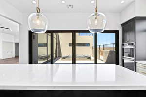 Kitchen with stainless steel double oven, light stone countertops, dark cabinets, recessed lighting, and decorative light fixtures