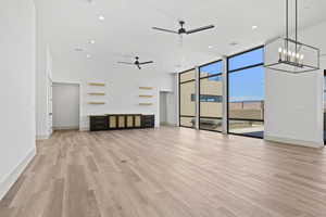 Unfurnished living room featuring a ceiling fan, a wall of windows, light wood-type flooring, recessed lighting, and a chandelier