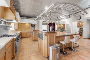 Kitchen featuring a large island, high end stove, a warming drawer, a kitchen bar, and custom exhaust hood