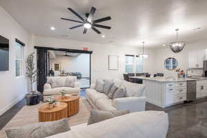 Living room featuring a ceiling fan, recessed lighting, a chandelier, and finished concrete floors