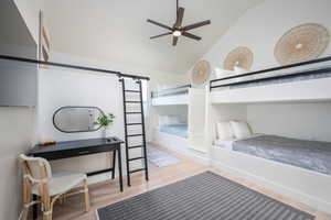 Bedroom with wood finished floors, a barn door, and high vaulted ceiling