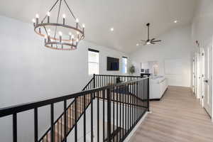 Hallway featuring an upstairs landing, light wood-style flooring, high vaulted ceiling, a chandelier, and recessed lighting