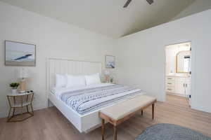 Bedroom with vaulted ceiling, light wood-type flooring, ensuite bath, and a ceiling fan