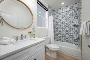 Bathroom featuring shower / bathtub combination with curtain, vanity, wood finished floors, and recessed lighting