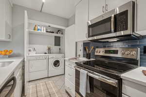Kitchen with appliances with stainless steel finishes, independent washer and dryer, light countertops, white cabinetry, and backsplash
