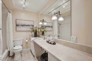 Bathroom featuring vanity, rail lighting, shower / tub combo, ornamental molding, and stone tile flooring