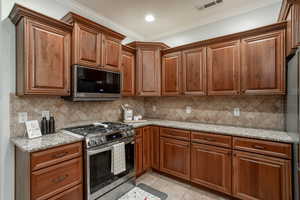 Kitchen featuring appliances with stainless steel finishes, crown molding, light tile patterned floors, and brown cabinetry
