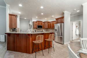 Kitchen with stainless steel appliances, a peninsula, light stone countertops, decorative backsplash, and a kitchen bar