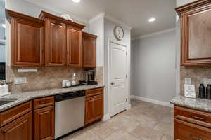Kitchen with dishwasher, crown molding, light stone countertops, backsplash, and brown cabinets