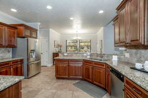 Kitchen with stainless steel appliances, a chandelier, decorative backsplash, a peninsula, and recessed lighting