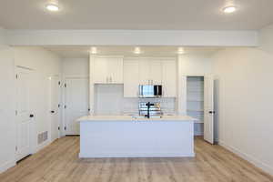 Kitchen with appliances with stainless steel finishes, light wood-type flooring, light countertops, white cabinetry, and a kitchen island with sink