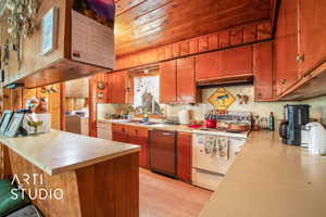 Kitchen featuring white appliances, washing machine and dryer, light countertops, brown cabinets, and a peninsula
