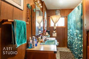 Bathroom featuring a textured ceiling, vanity, wooden walls, and a shower with shower curtain