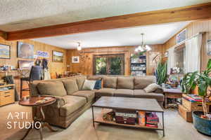 Carpeted living area with wooden walls, a textured ceiling, beamed ceiling, and a chandelier