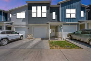 Multi unit property featuring a garage, driveway, stone siding, and board and batten siding