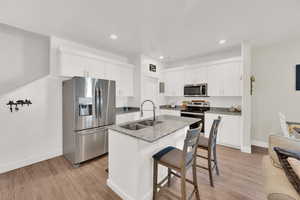 Kitchen with appliances with stainless steel finishes, light wood finished floors, a kitchen breakfast bar, recessed lighting, and light stone countertops
