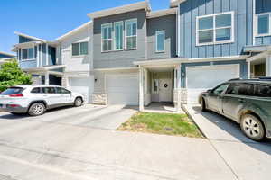 Multi unit property featuring an attached garage, driveway, board and batten siding, and stone siding