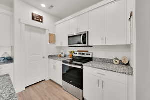 Kitchen featuring appliances with stainless steel finishes, light wood-style floors, white cabinets, recessed lighting, and light stone countertops