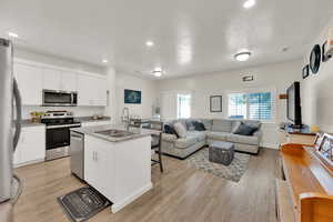 Kitchen with stainless steel appliances, light wood finished floors, open floor plan, a kitchen island with sink, and white cabinetry