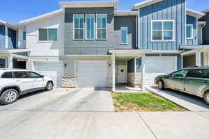 Townhome / multi-family property with a garage, driveway, stone siding, and board and batten siding