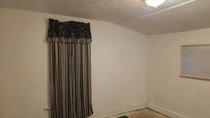 Empty room featuring vaulted ceiling and a textured ceiling