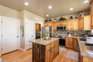 Kitchen with stainless steel appliances, washer / dryer, backsplash, light wood finished floors, and recessed lighting