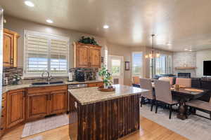 Kitchen featuring light wood-type flooring, a textured ceiling, a stone fireplace, tasteful backsplash, and recessed lighting