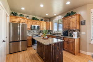 Kitchen with appliances with stainless steel finishes, light wood-style flooring, light stone counters, tasteful backsplash, and a kitchen island