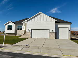 View of front facade with board and batten siding, stone siding, a front yard, concrete driveway, and an attached garage