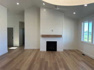 Living room featuring a ceiling fan, lofted ceiling, light wood-type flooring, a large fireplace, and recessed lighting