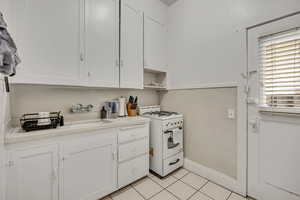 Kitchen with white gas range, white cabinets, light countertops, and light tile patterned floors