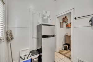 Kitchen with freestanding refrigerator, white microwave, and light tile patterned floors