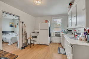 Kitchen featuring white appliances, light wood-style flooring, light countertops, cooling unit, and white cabinetry