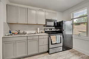 Kitchen with black appliances, gray cabinets, tasteful backsplash, light wood-type flooring, and light countertops