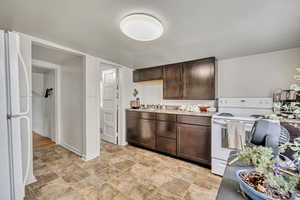 Kitchen with white appliances, dark brown cabinetry, light countertops, and stone finish floors