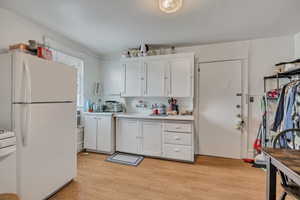 Kitchen with freestanding refrigerator, light countertops, white cabinets, stove, and light wood-type flooring