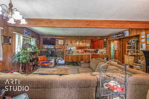Living room featuring wooden walls, beamed ceiling, a chandelier, a textured ceiling, and a fireplace