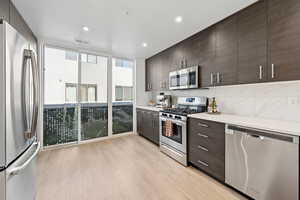 Kitchen with appliances with stainless steel finishes, dark brown cabinetry, light countertops, backsplash, and light wood-style floors