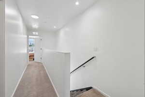 Hall with an upstairs landing, light colored carpet, and recessed lighting