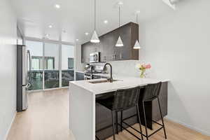Kitchen featuring stainless steel appliances, light countertops, a kitchen breakfast bar, light wood finished floors, and a peninsula