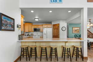 Kitchen with white appliances, a peninsula, light countertops, recessed lighting, and a kitchen bar
