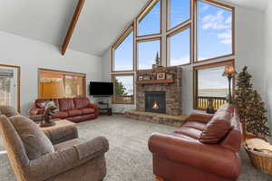 Carpeted living area with high vaulted ceiling, a fireplace, and beam ceiling